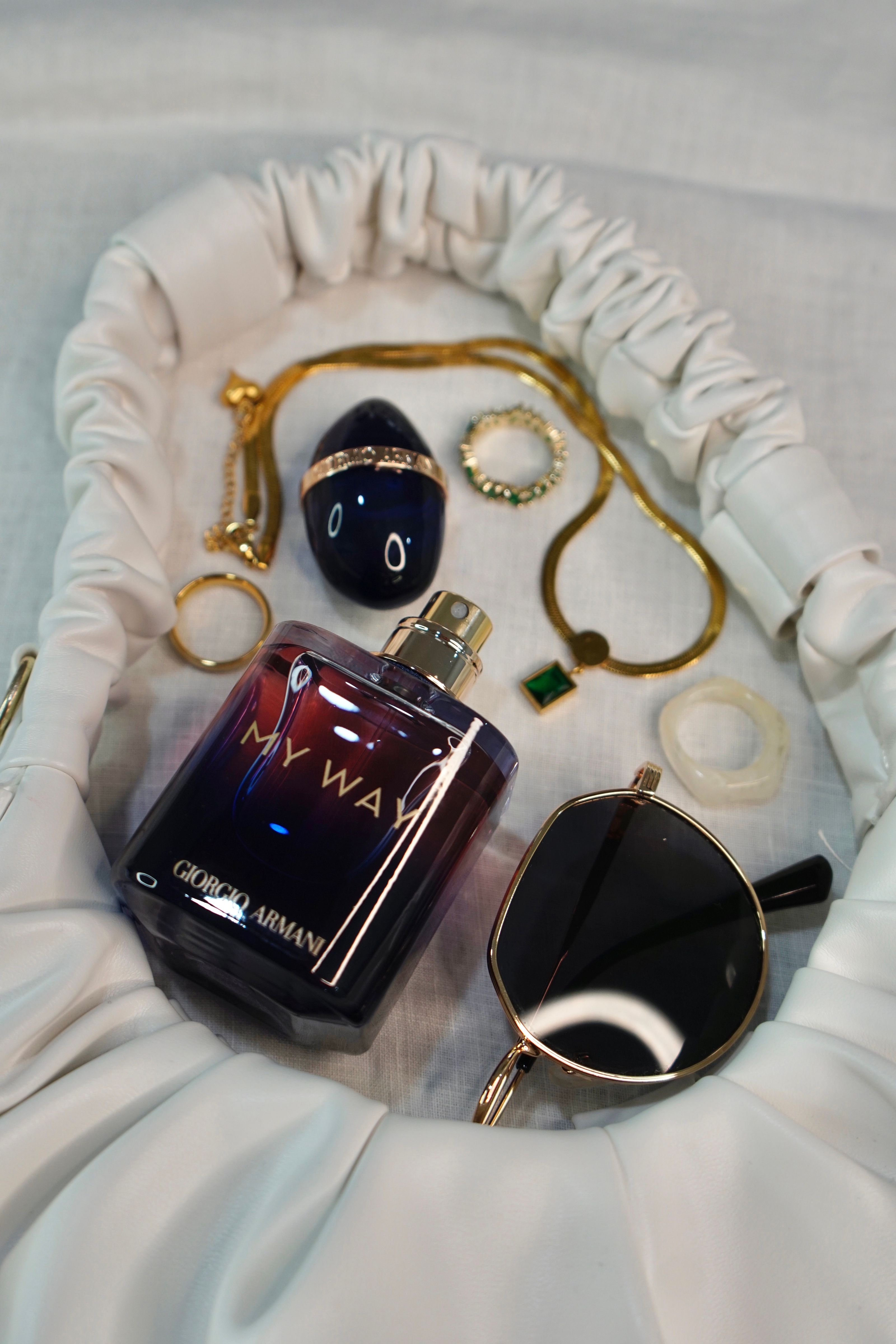 Disposição estilosa de perfume e acessórios sobre tecido, destacando a elegância.