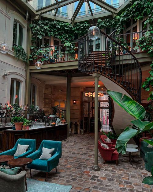 Free Luxurious hotel lobby featuring a spiral staircase, lush plants, and cozy seating under a glass ceiling. Stock Photo