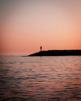 A serene silhouette of a man standing on a pier against a warm sunset sky over the sea.