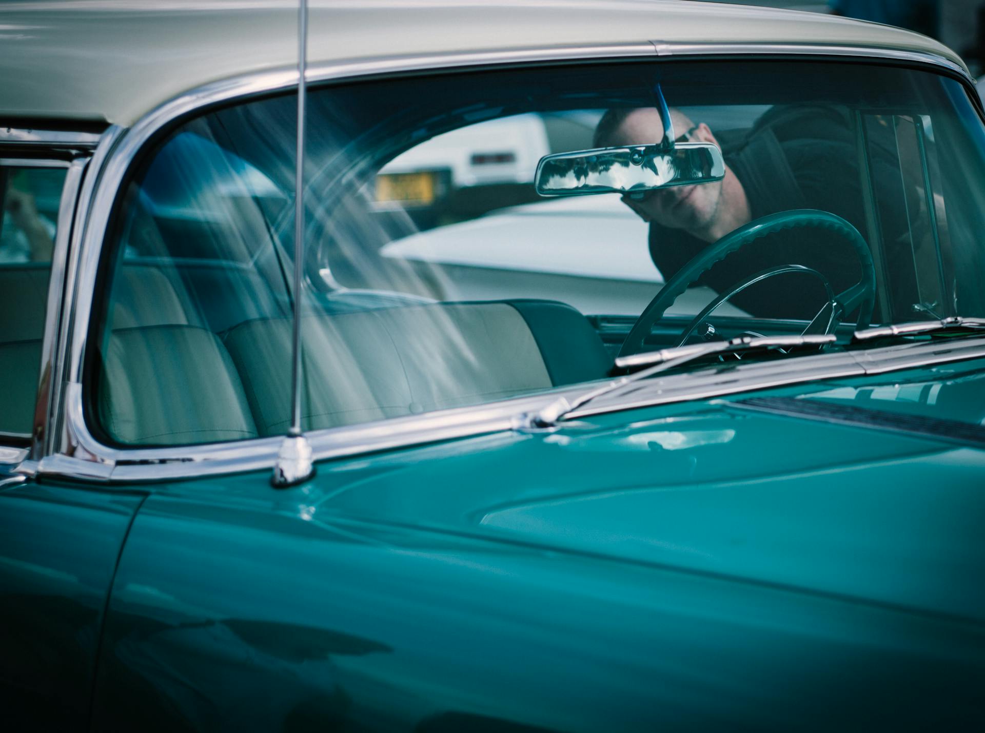 Close-up of a vintage car with a man visible in the rearview mirror, emphasizing classic and elegant design.