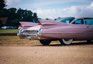 在一个阳光明媚的日子里，一辆老式粉红色凯迪拉克停放着，展示着它标志性的尾鳍