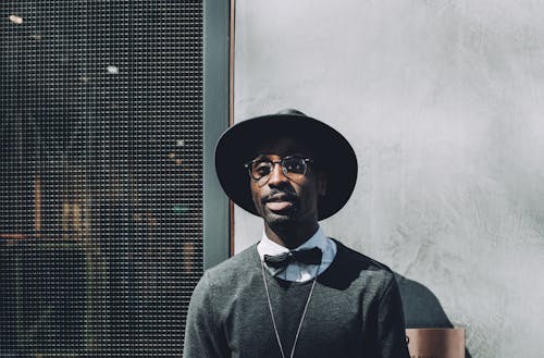 Man Wearing Hat and Bowtie in Front of Concrete Wall