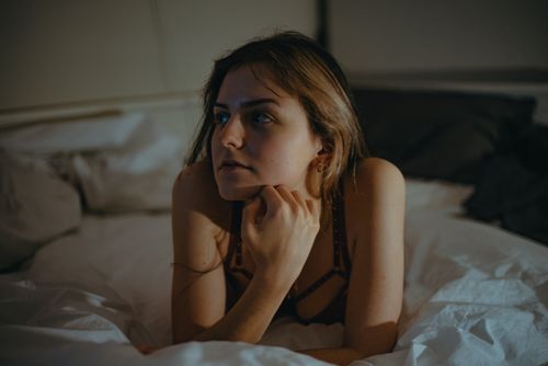 Free A contemplative young woman in lingerie relaxes on a bed in serene lighting. Stock Photo