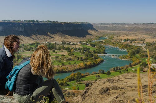 Two People Seated Facing Body of Water and Mountains