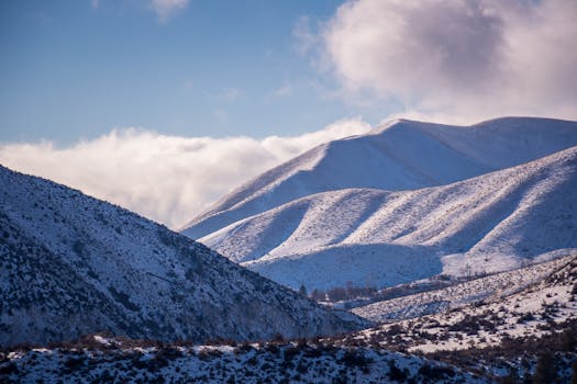 Breathtaking view of snow-covered mountains with clouds and blue sky backdrop.