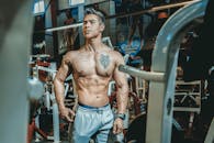 在健身房环境中，一名赤裸上身、纹身的男子摆出姿势，展示着健康和力量