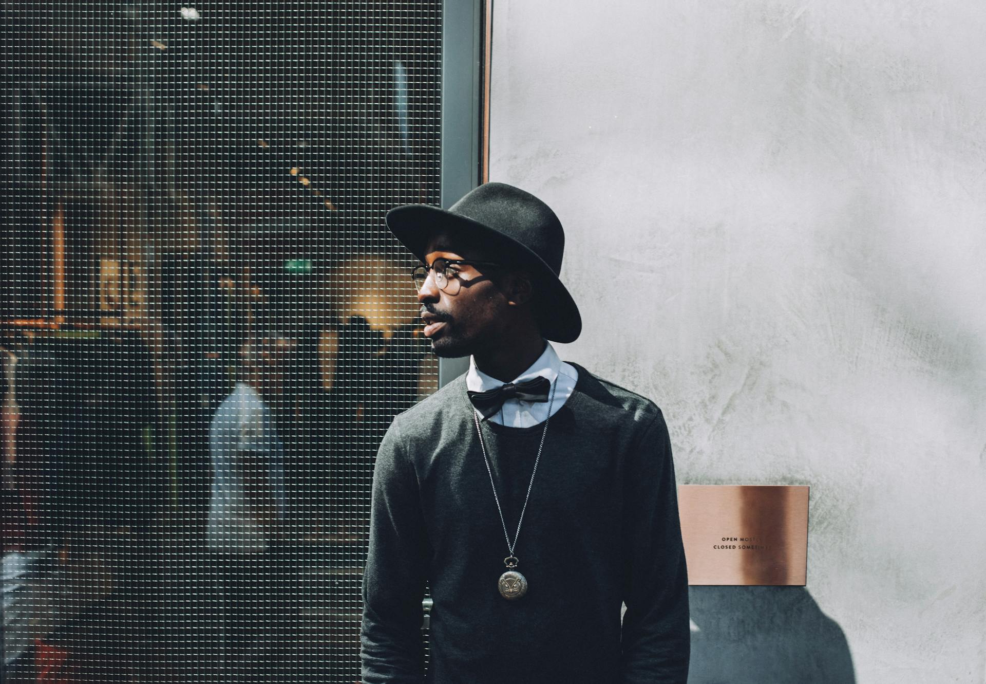 Chic portrait of a fashionable man wearing a hat and bow tie against a textured wall.