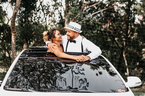 Free Newlywed couple smiling from a car sunroof, surrounded by lush greenery, capturing love and happiness. Stock Photo