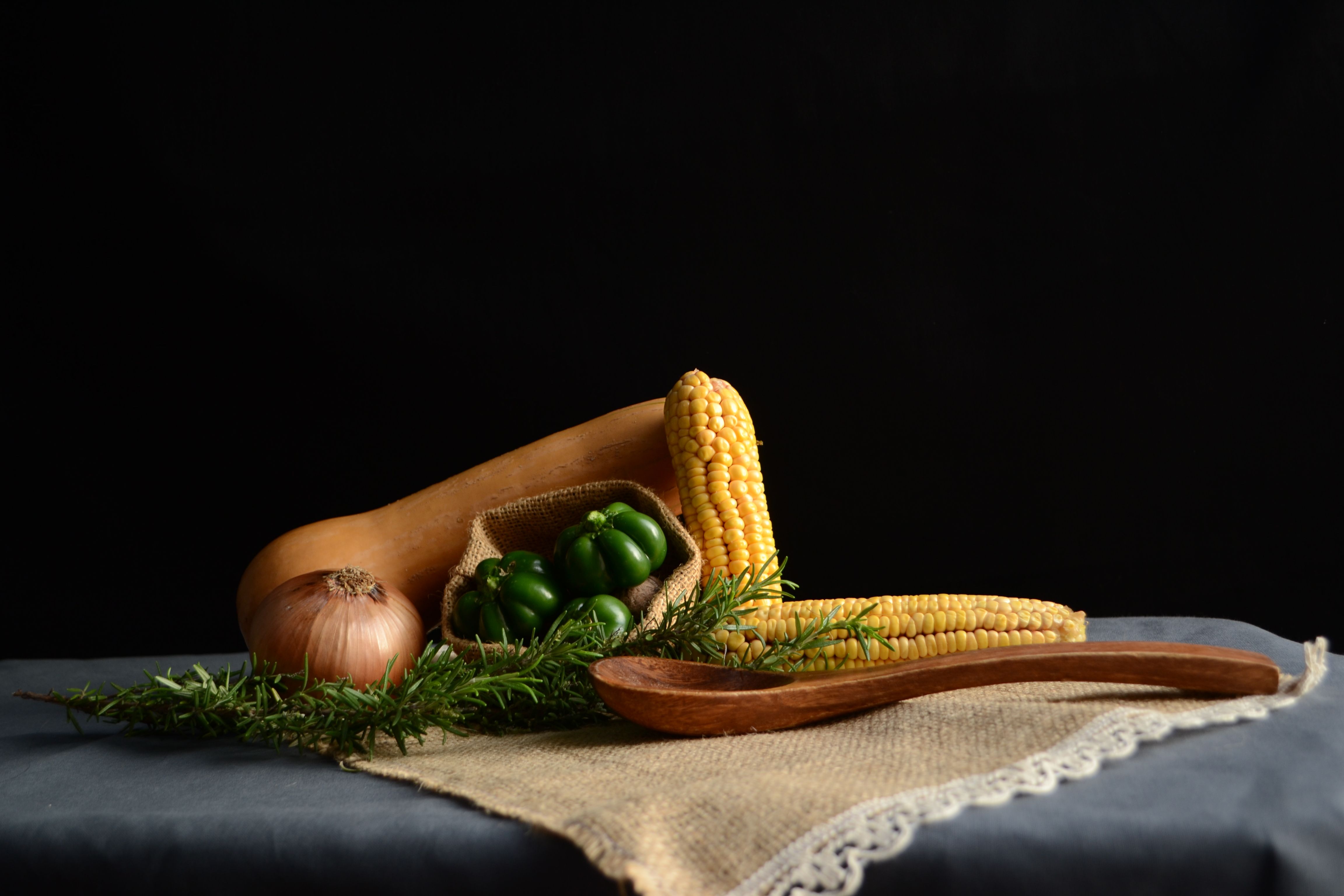 A rustic display of vegetables including corn, bell pepper, and squash on burlap.