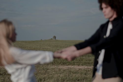 Free Blurry image of a couple holding hands in a serene rural meadow under a clear sky. Stock Photo