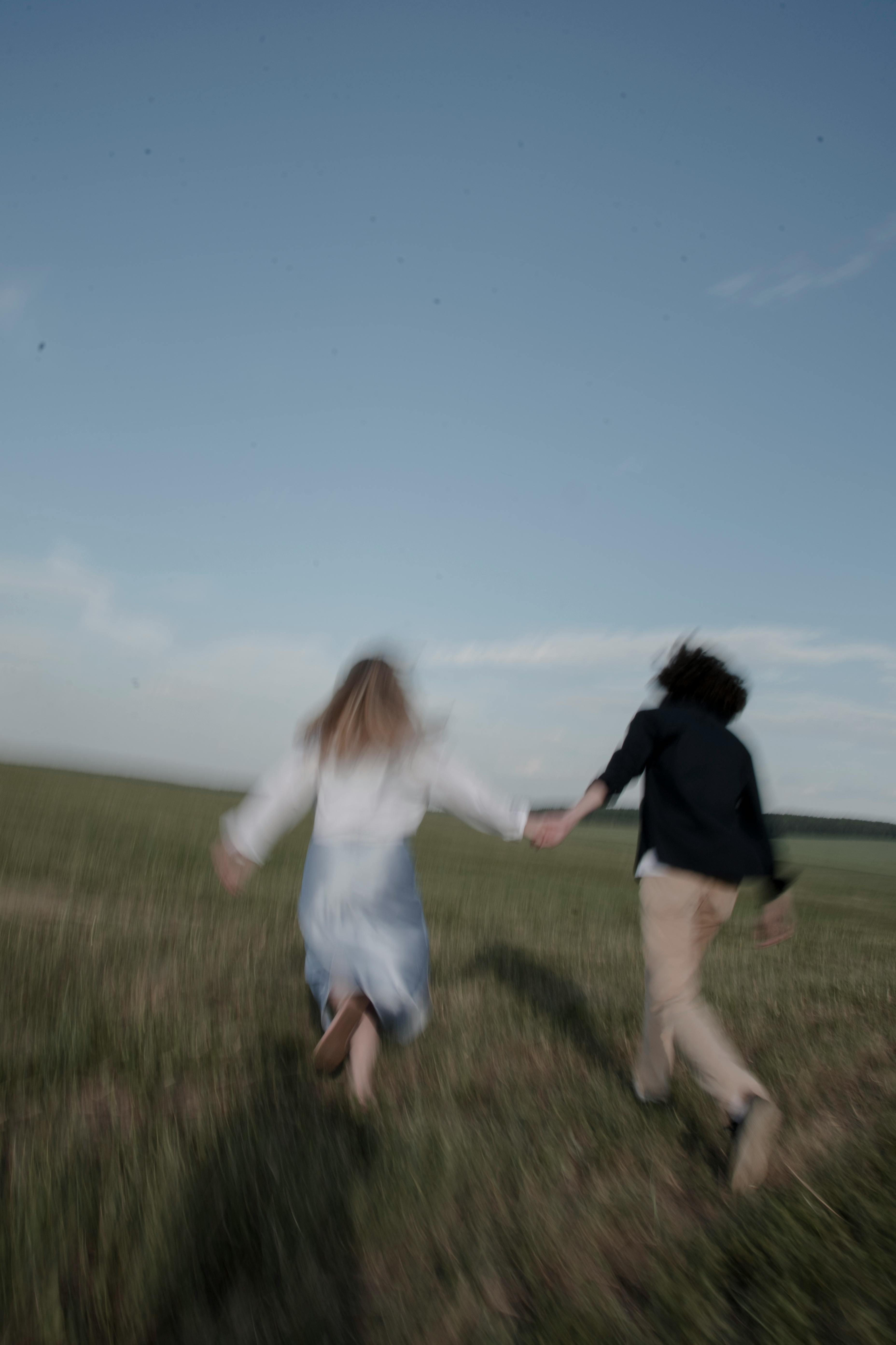 Blurred motion of a couple holding hands and running through a serene grassy field during the day.