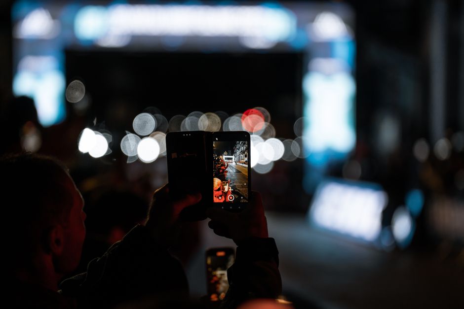 スマートフォンを使って夜の都市シーンを撮影している人物、活気ある街の明かりが映える。
