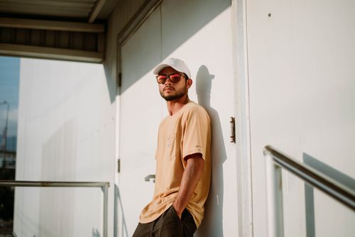 Free Man in sunglasses leaning against a white door, showcasing casual summer fashion. Stock Photo