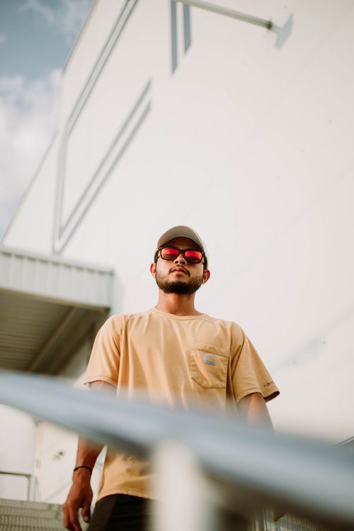 Free Confident young man wearing sunglasses and a cap, standing outdoors against a modern building. Stock Photo