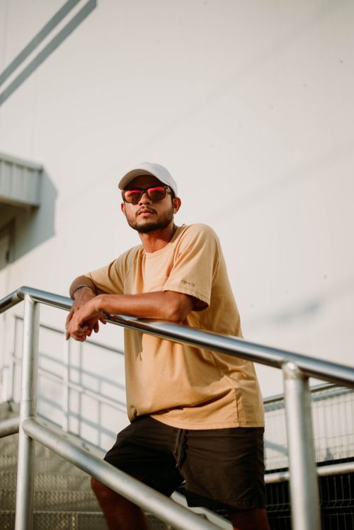 Free Stylish man wearing sunglasses and a cap leaning on a railing in an urban setting. Stock Photo