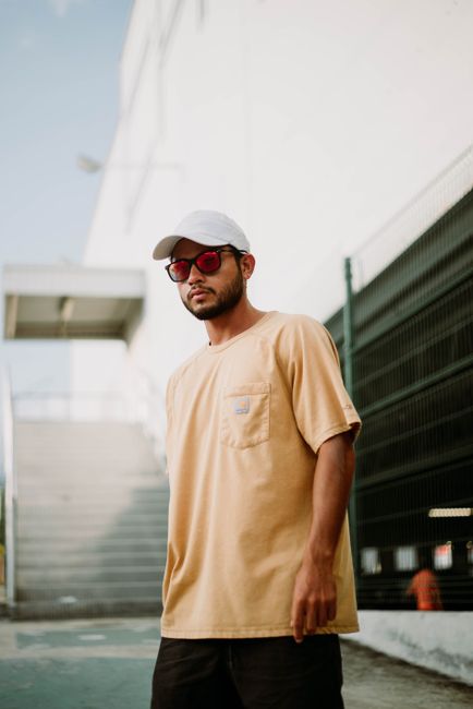 Stylish man in a yellow shirt and sunglasses posing outdoors in urban setting.