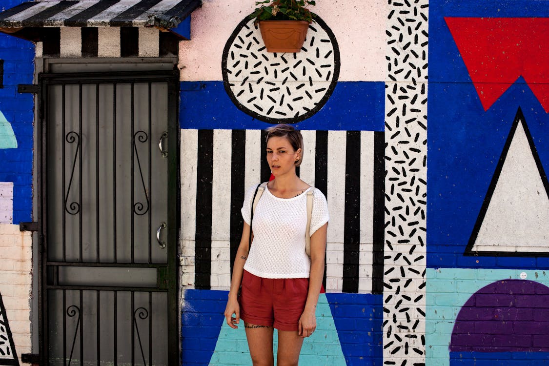 無料 塗られた壁の近くに立っている白いトップの女性 写真素材