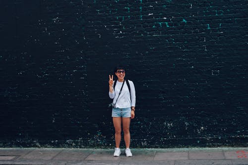 Woman in Blue Denim Shorts Standing in Front of Black Brick Wall