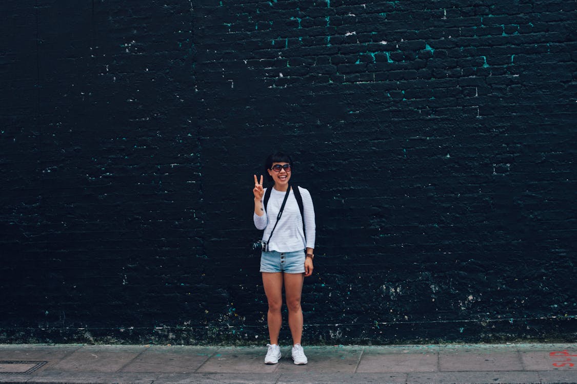 Free Woman in Blue Denim Shorts Standing in Front of Black Brick Wall Stock Photo