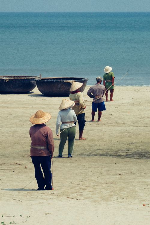Free Fishermen on a Vietnamese beach with traditional conical hats preparing for work. Stock Photo