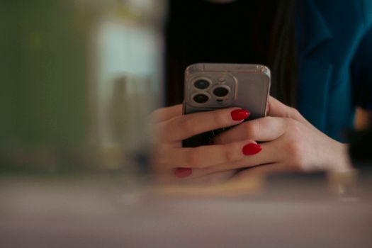 Close-up shot of a woman texting on a smartphone indoors, showcasing red nail polish.