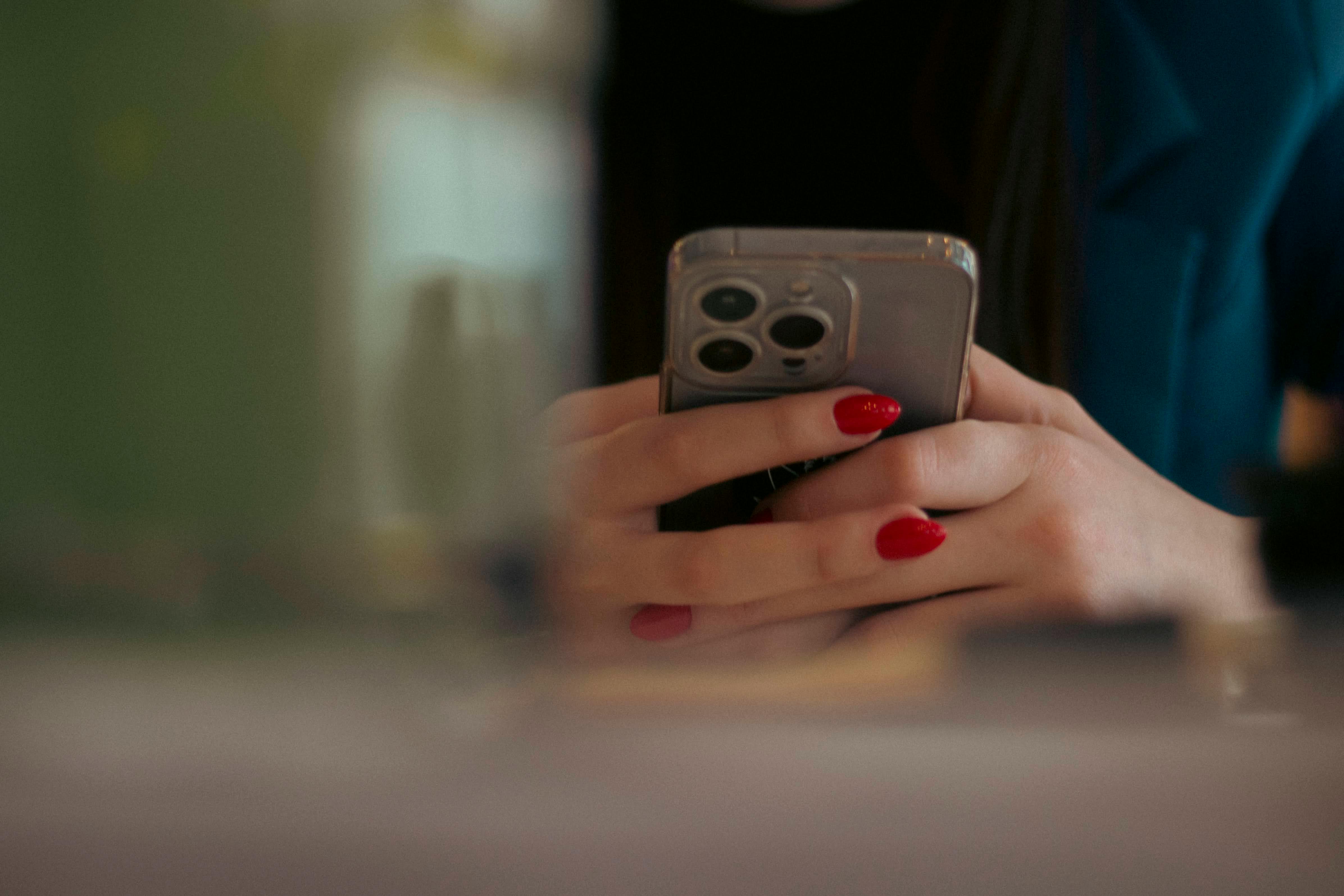 Free Close-up shot of a woman texting on a smartphone indoors, showcasing red nail polish. Stock Photo