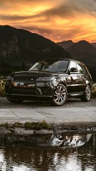 A sleek SUV parked by a tranquil lake with a mountain backdrop during a vibrant sunset.