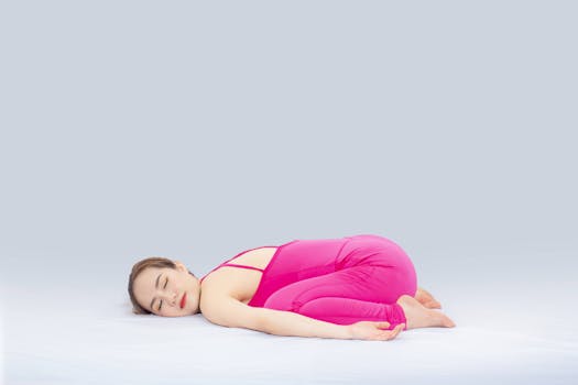 Woman doing yoga indoors in a pink outfit, demonstrating the child's pose for wellness and relaxation.