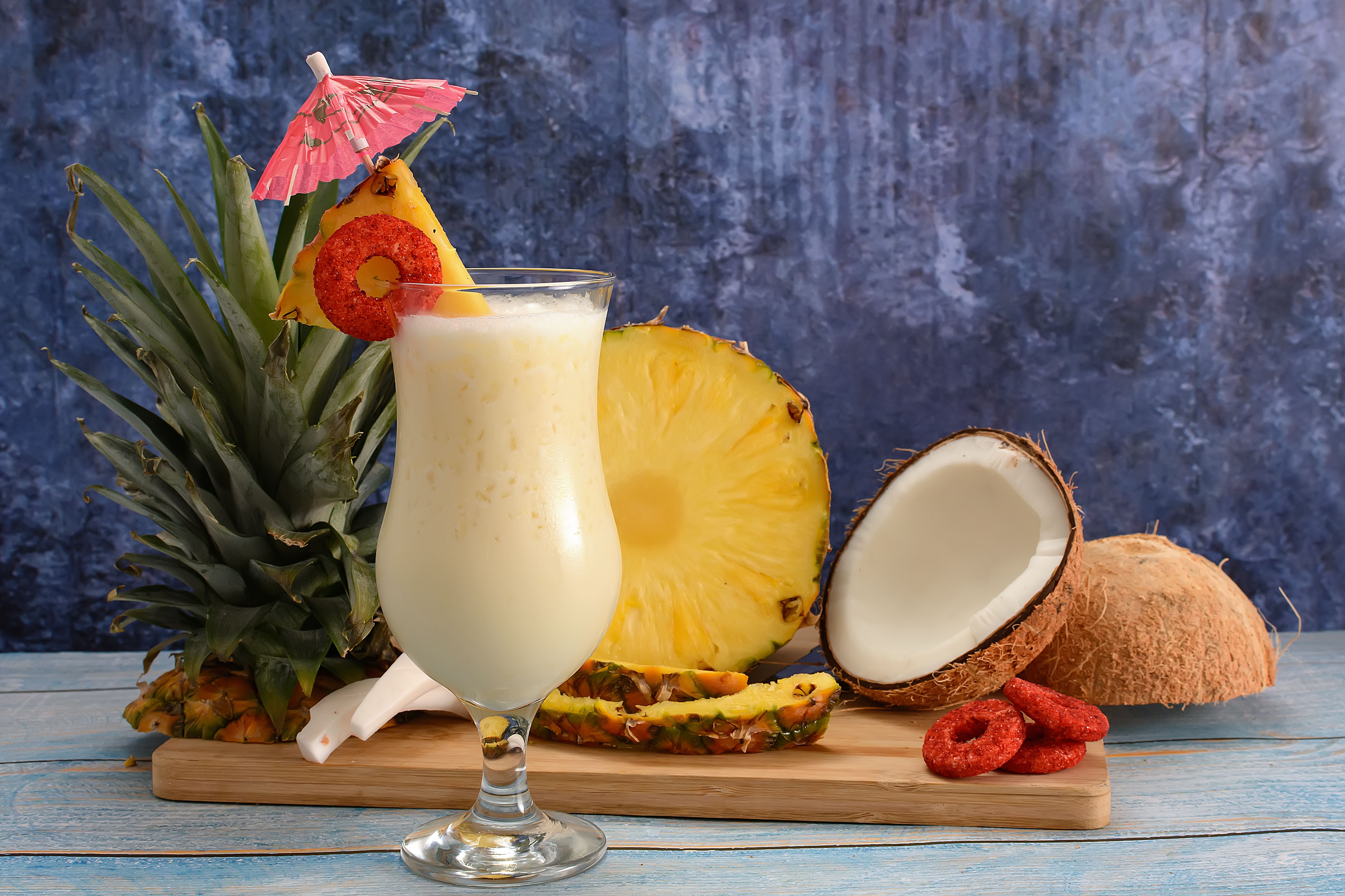 Free Pina colada, tropical cocktail. Glass of pina colada on a blue wooden table with the components of the cocktail in the background. Stock Photo
