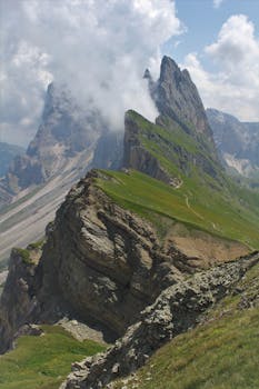 Majestic view of grassy slopes and jagged peaks of Seceda in the Italian Alps under a cloudy sky.