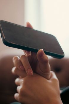 Close-up of a woman's hands with manicured nails holding a smartphone indoors, highlighting technology and connectivity.