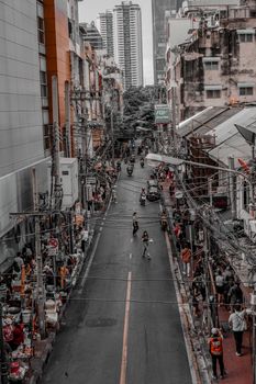 A busy street scene capturing people and scooters in an Asian city with tall buildings around.