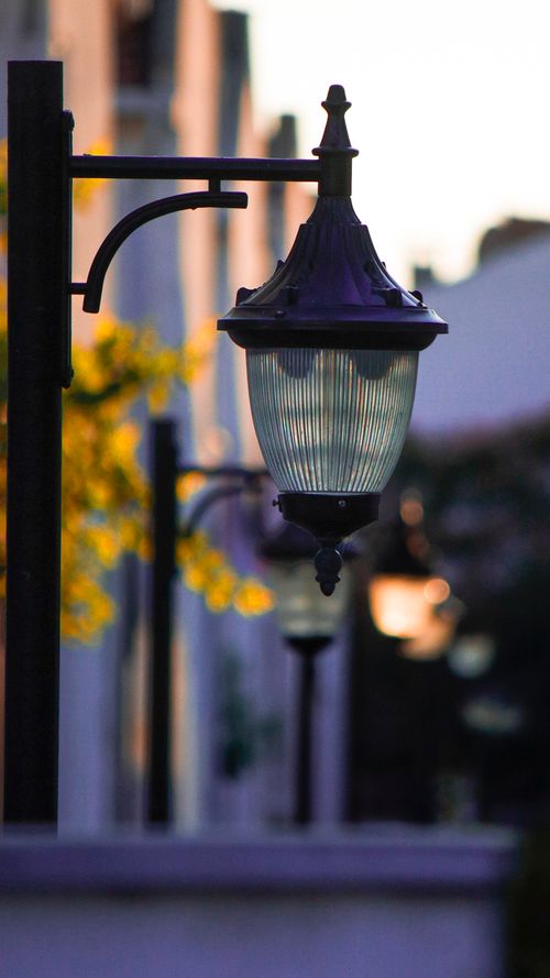 Free Vertical shot of vintage street lamps lining a street at sunset, casting warm light. Stock Photo