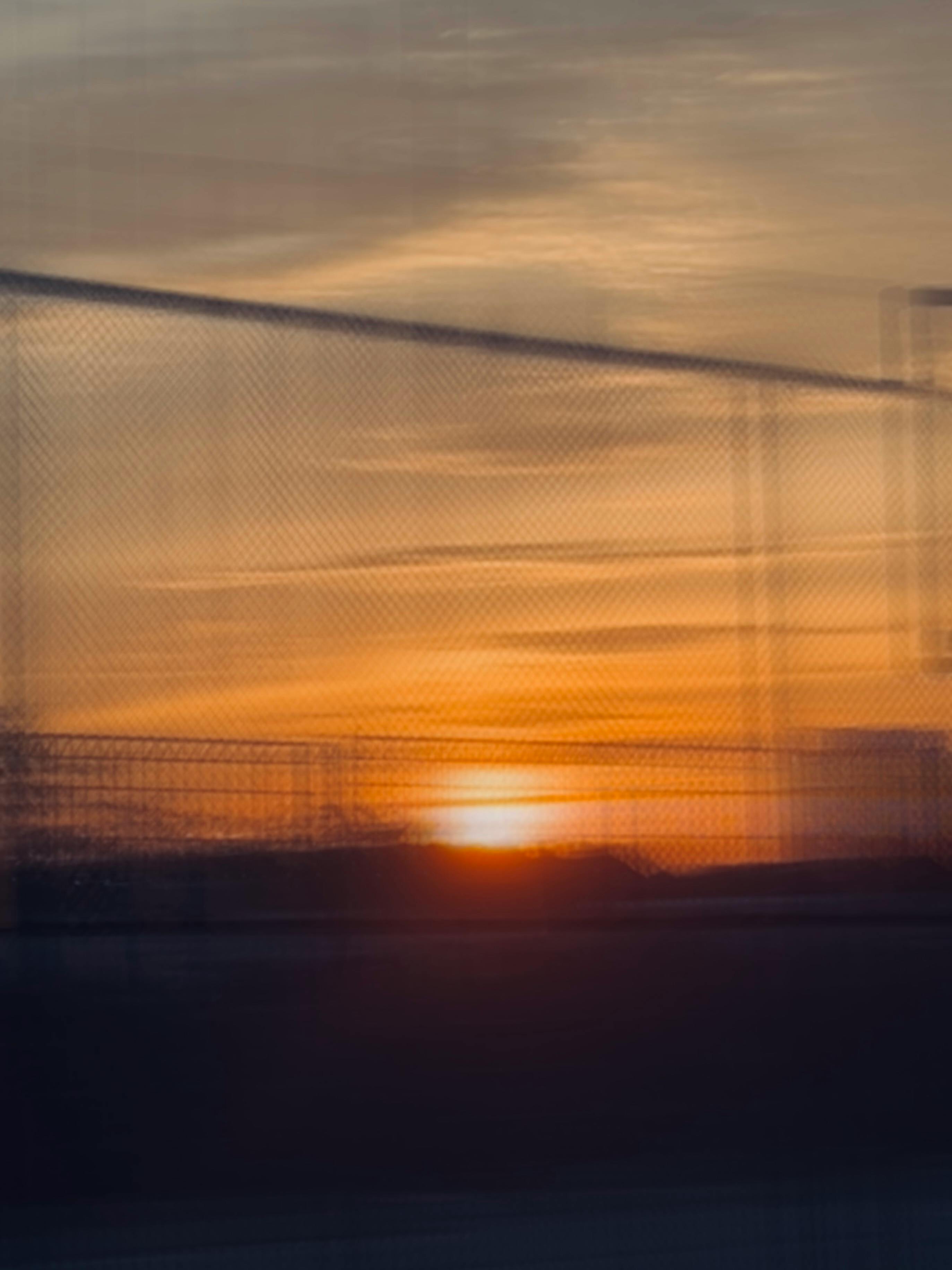 A blurred motion capture of a beautiful sunset behind a chain-link fence.