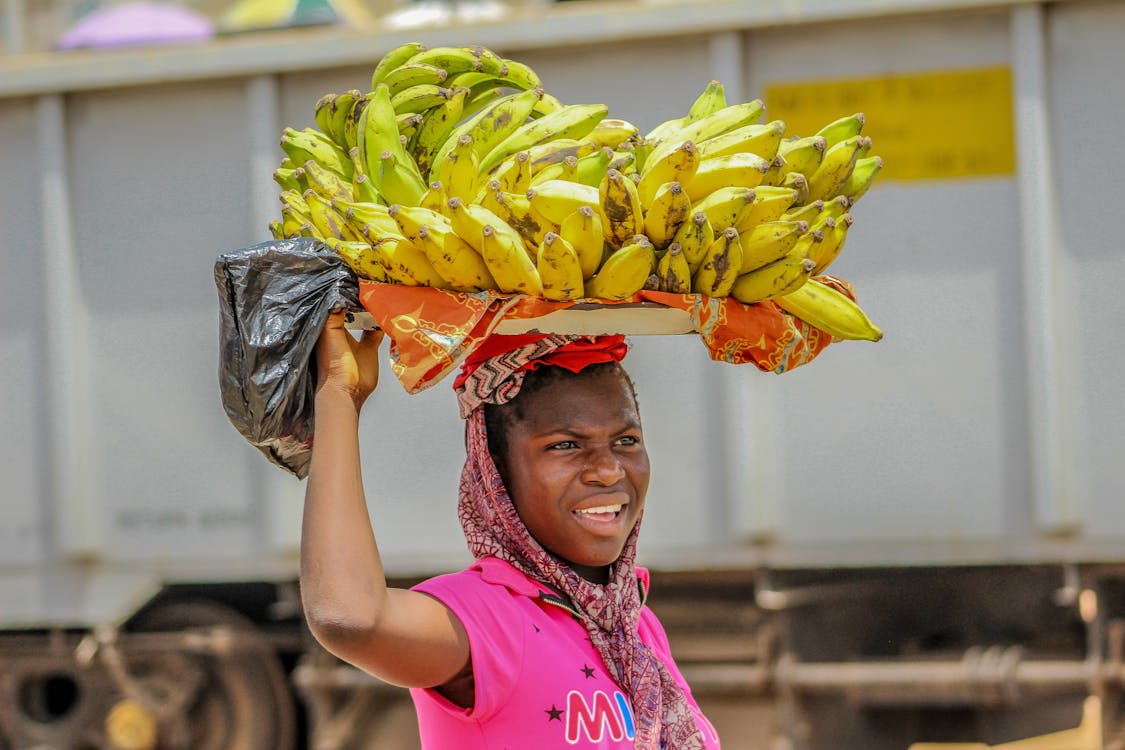 Person in Pink Top Carrying Cluster of Bananas