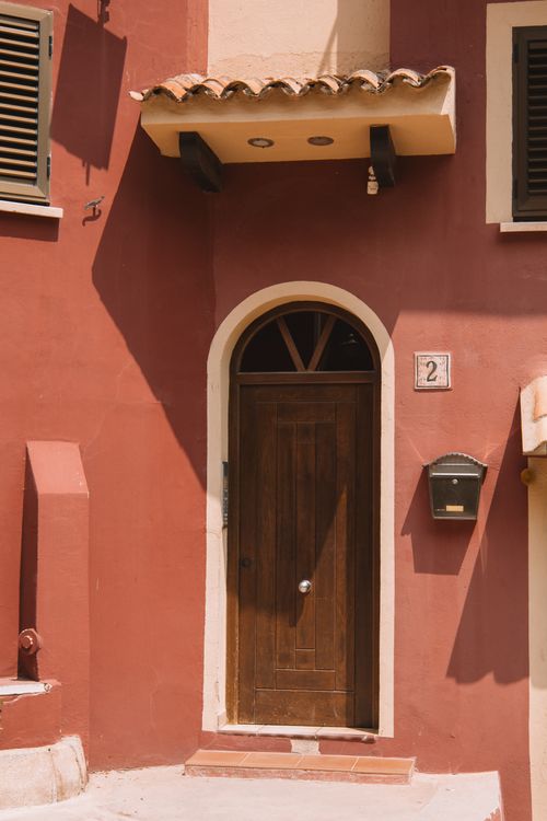 Free Rustic wooden door on a sunlit red building facade in Valencia, Spain, showcasing Mediterranean architecture. Stock Photo