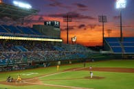 在拥挤的体育场内，一场充满活力的棒球比赛在令人惊叹的日落天空下进行
