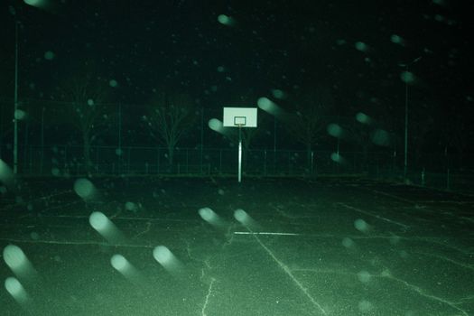 Abandoned basketball court at night with fog creating a moody, eerie atmosphere.