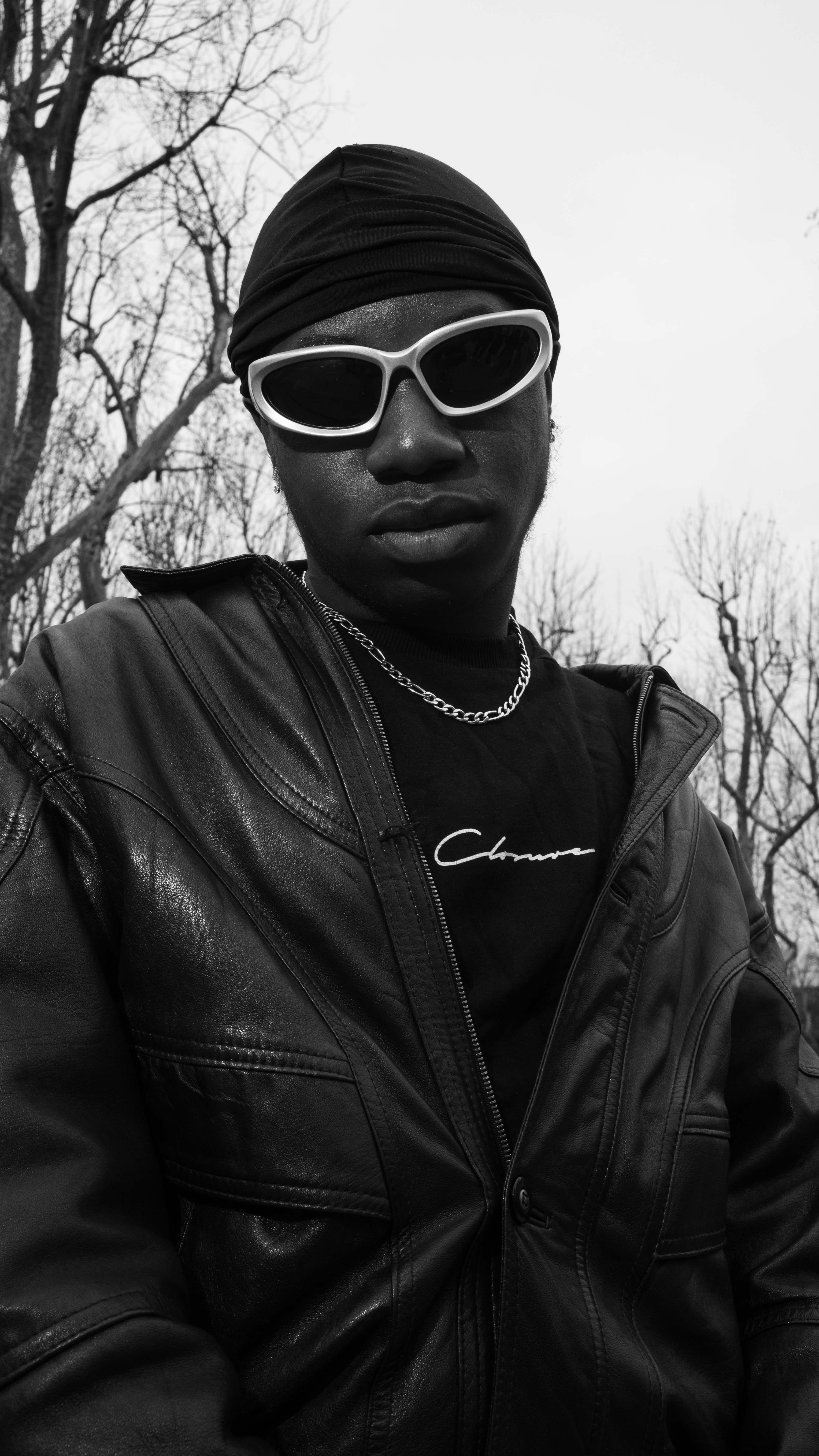 Fashionable black and white portrait featuring leather jacket and sunglasses in an outdoor setting.