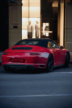 Sleek red sports car on a city street at dusk, with mannequins visible in a storefront.