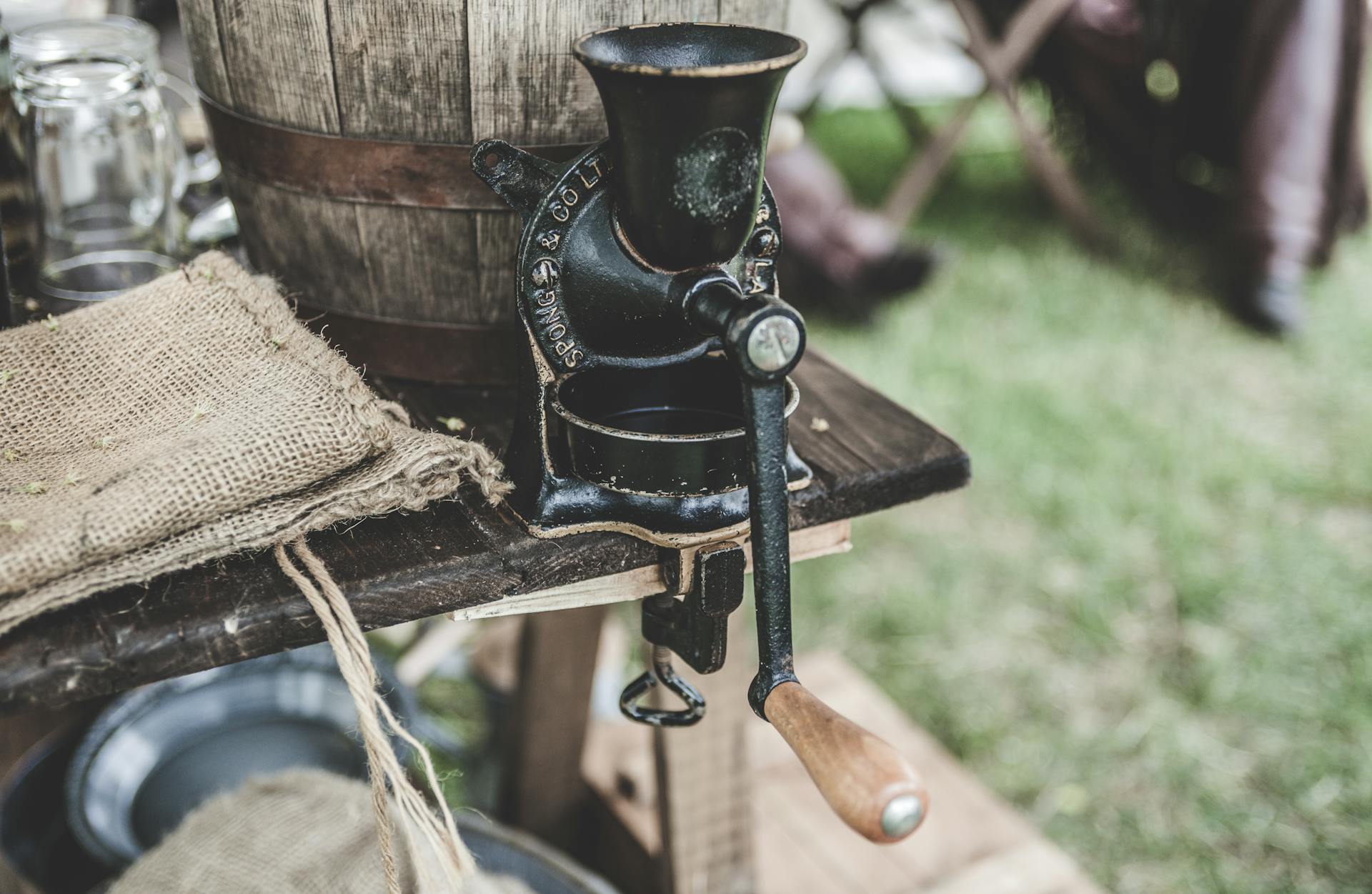 A rustic vintage coffee grinder on a wooden table with burlap sack outdoors.