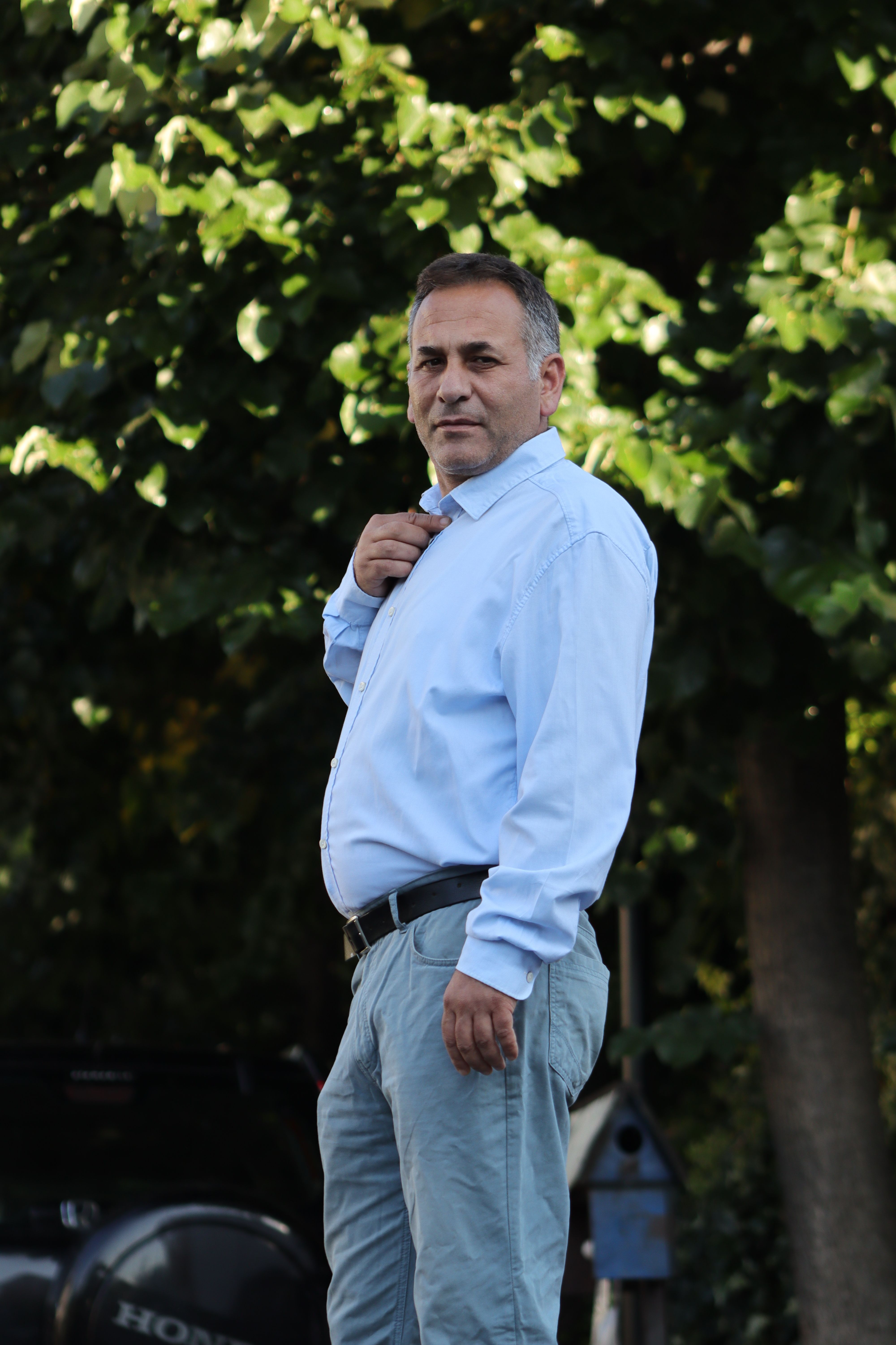 Stylish man in casual shirt poses confidently in lush outdoor setting