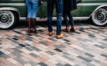 一辆经典绿色汽车旁的砖砌街道上，站着三位时尚人士