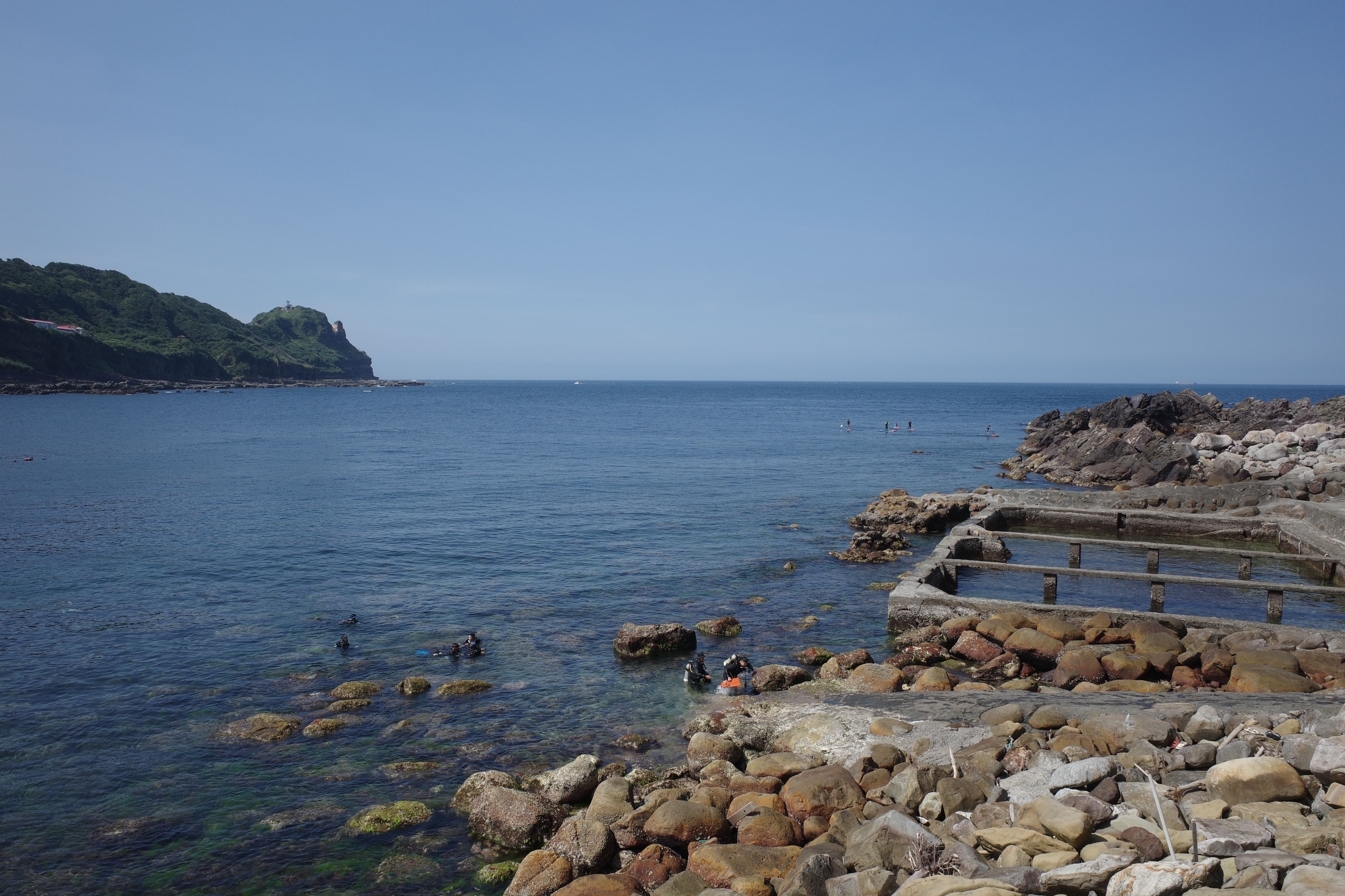 Explore the serene rocky coastline in Taipei, Taiwan, featuring clear waters and lush greenery.