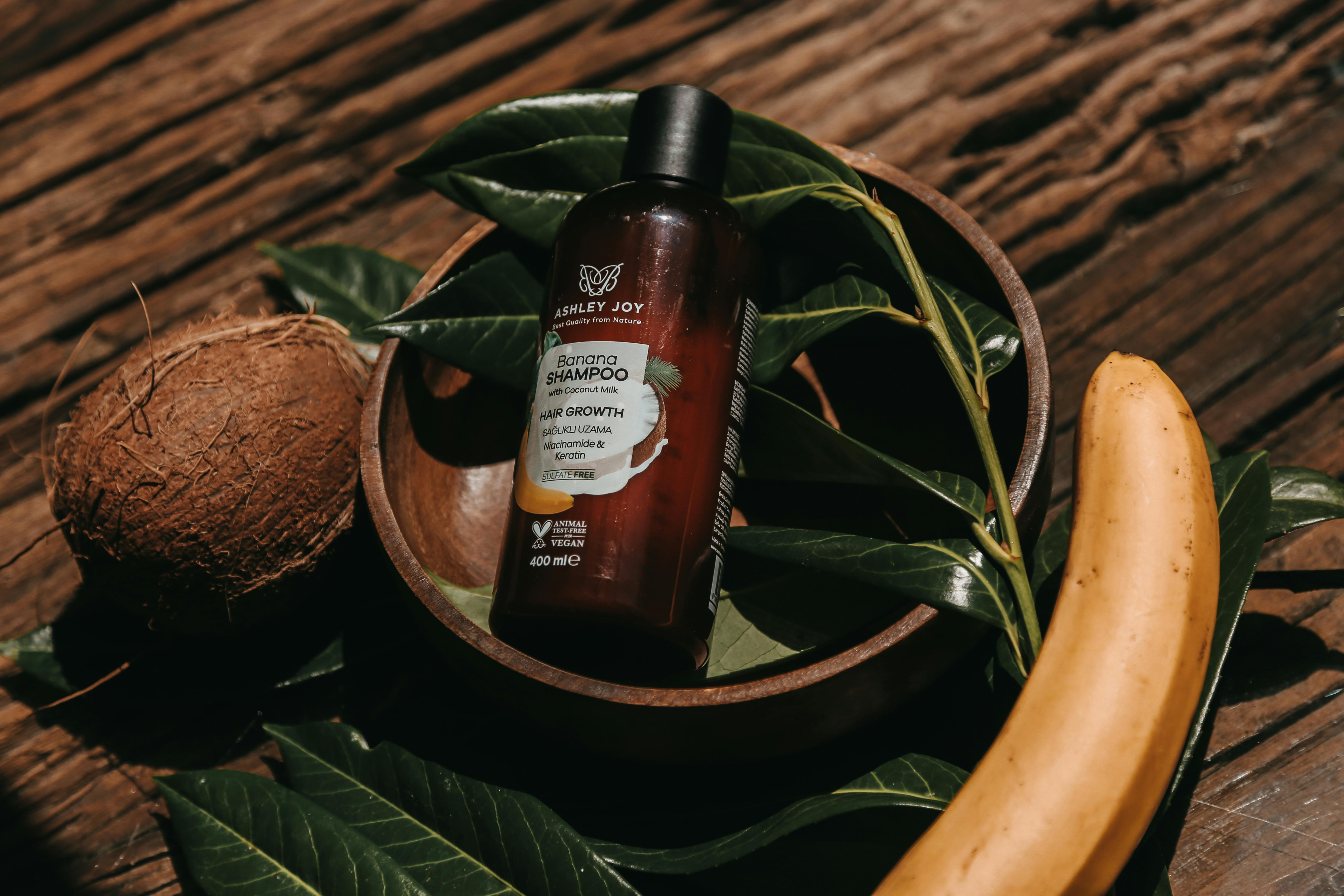 Natural shampoo bottle surrounded by banana and coconut on wooden surface.