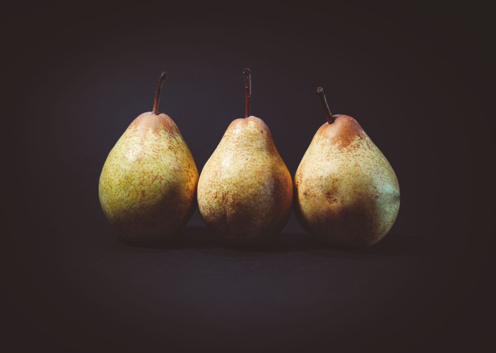 A close-up of three ripe pears displayed against a dark background, showcasing their natural texture and color.