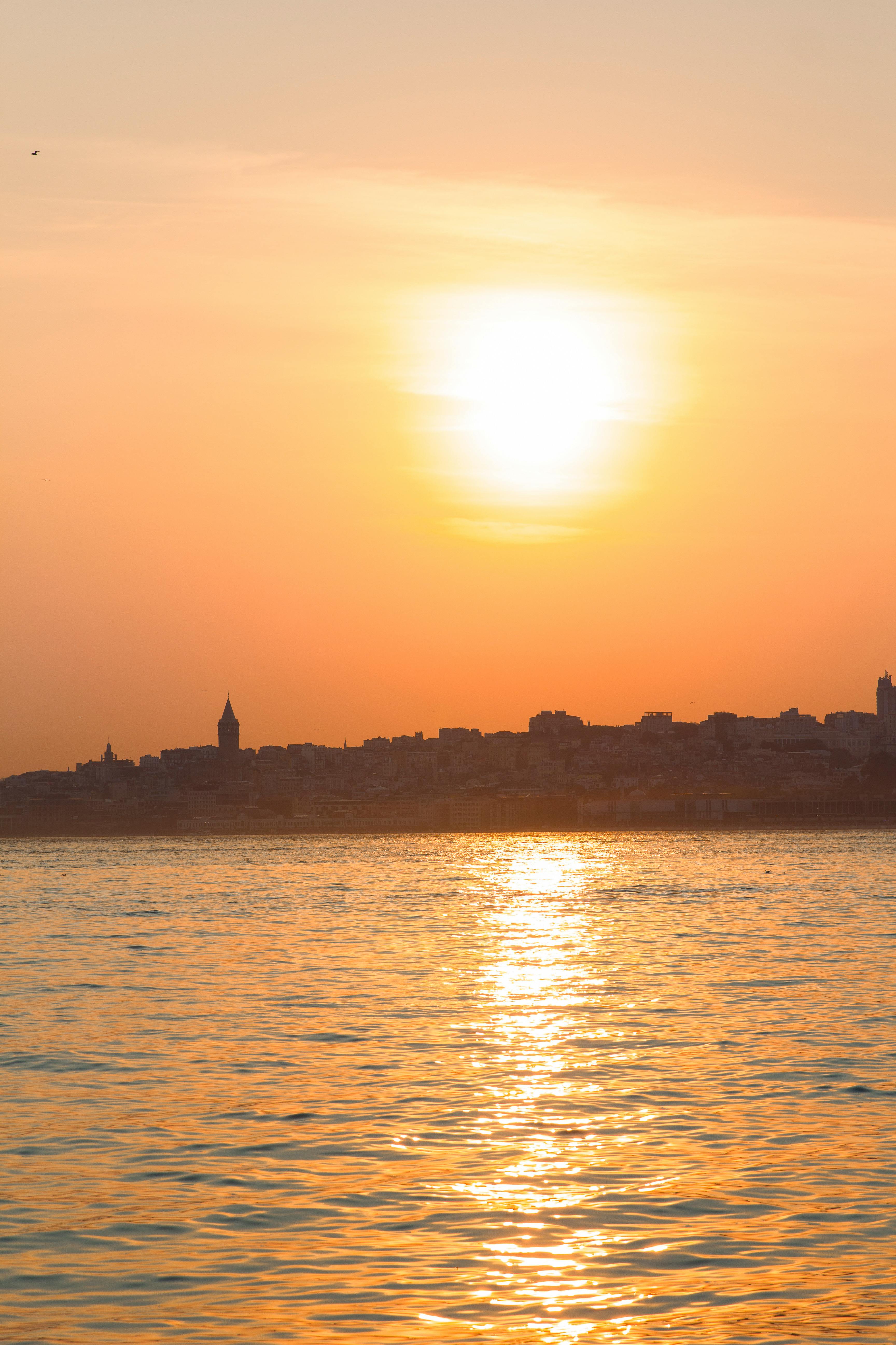A peaceful sunset over the sea with a silhouetted city skyline, reflecting vibrant colors.