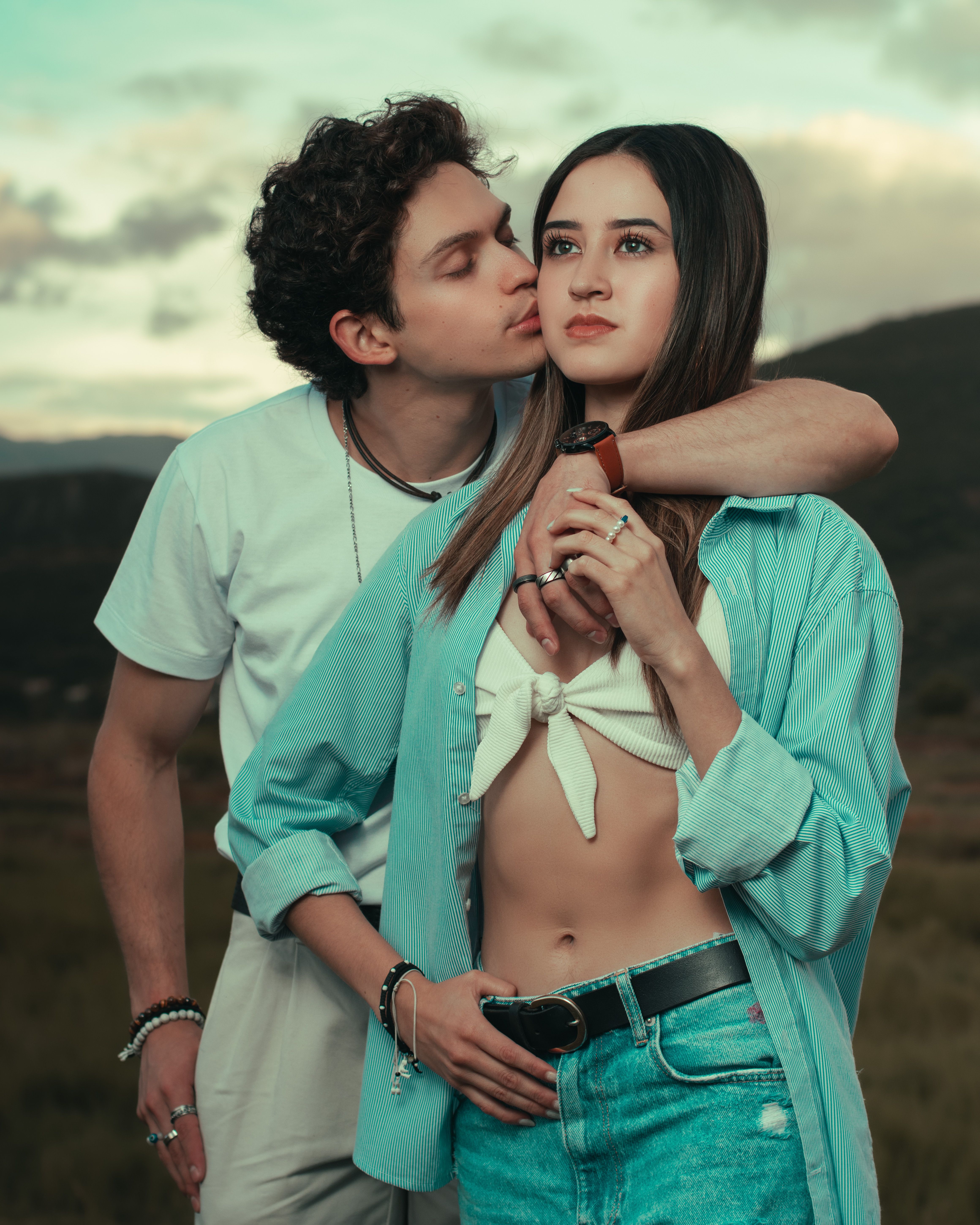 A young couple in casual outfits shares a tender moment outdoors, showcasing affection and connection.