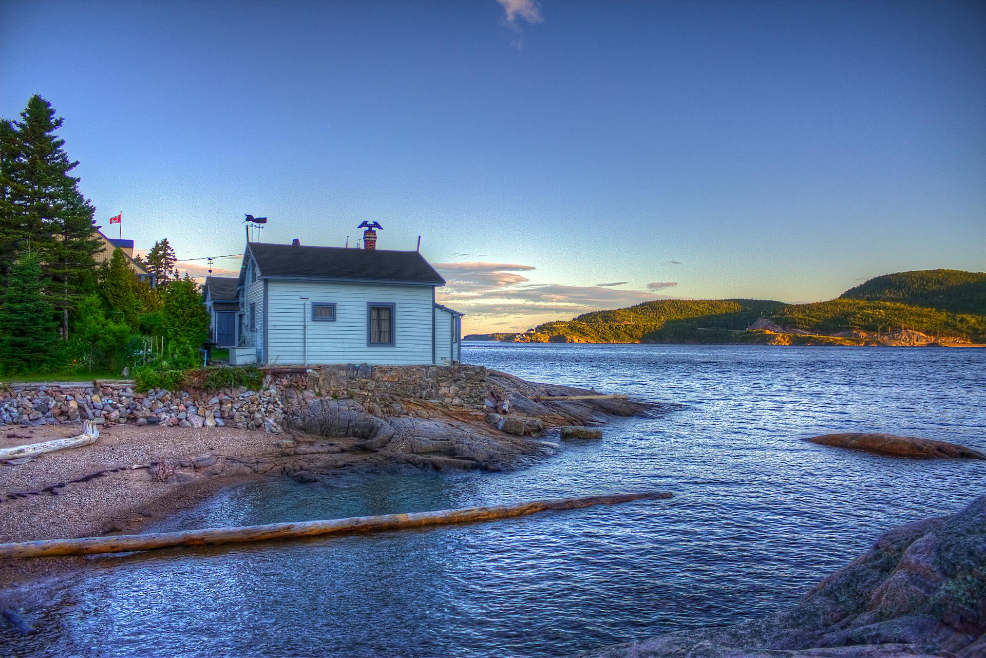 Charming lakeside cottage with mountain views in Tadoussac, Quebec at sunset.