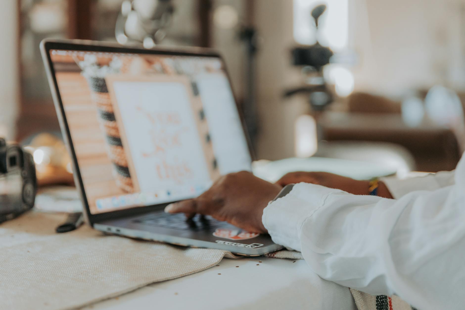 A person typing on a laptop with a blurred screen in a cozy home office setting.